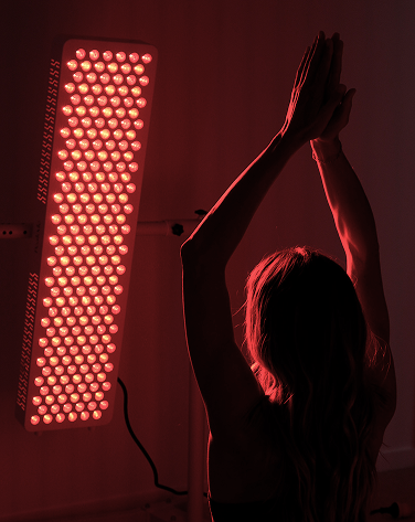 Person with arms raised in front of a red light panel on a dark background using PeakMe PRO Red Light Therapy panel