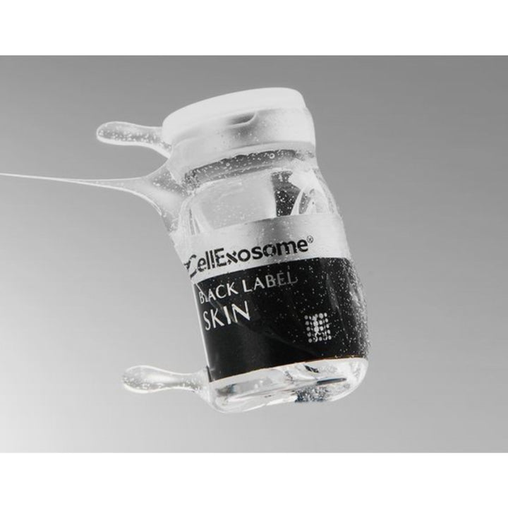 Close-up of a CellExosome BLACK LABEL Skin vial surrounded by serum droplets, highlighting the professional exosome skin regeneration treatment and premium skincare formulation.