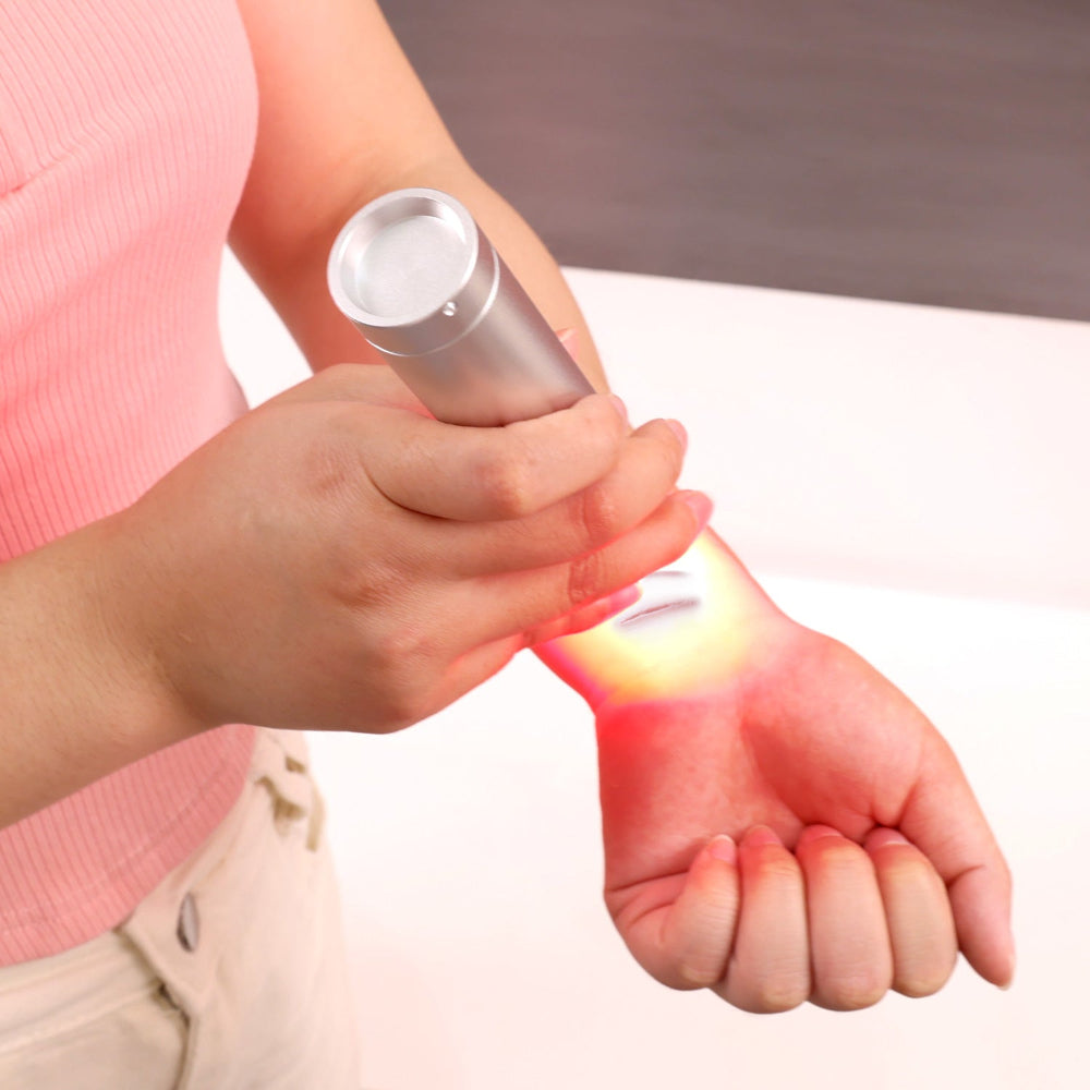 Handheld red light therapy torch being used on the wrist for targeted light application.